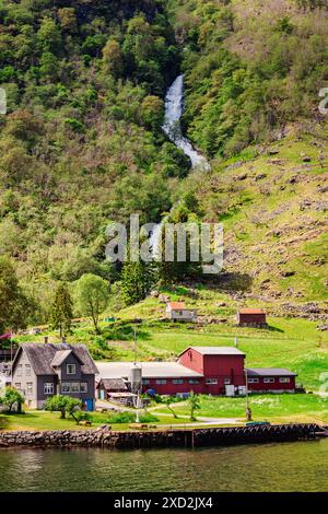 Un pittoresco paesaggio di un villaggio rurale con una cascata e lussureggianti colline verdi in Norvegia. Foto Stock