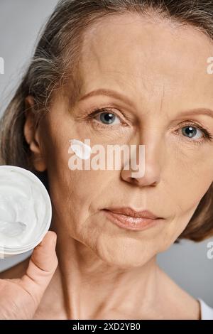 Una donna applica la crema al viso con cura e attenzione. Foto Stock