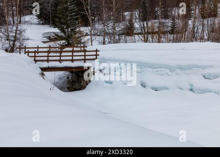 un ponte di legno attraversa il fiume nella valle innevata Foto Stock