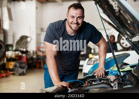 Meccanico, uomo e ritratto in auto in garage per la riparazione, la manutenzione e il sorriso per il controllo del motore. Ingegnere, persona e piccola impresa per veicoli Foto Stock