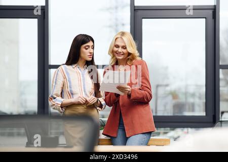 Due donne vestite professionalmente, in piedi in un ufficio di fronte a una grande finestra. Foto Stock