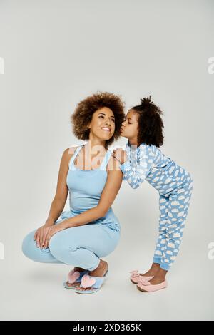 Un momento affettuoso tra una madre e una figlia afroamericana gioiosa, che indossa pigiami blu abbinati, che condividono un bacio. Foto Stock