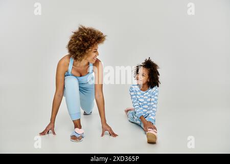 Allegra madre e figlia afroamericana in pigiama che praticano yoga insieme su un tranquillo sfondo bianco. Foto Stock