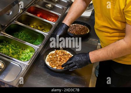 Lo chef mette le patatine fritte su una pizza nella cucina del ristorante con dettagli motivanti Foto Stock