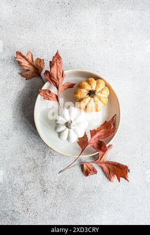 Un piatto autunnale splendidamente disposto con un piatto in ceramica con mini zucche bianche e arancioni, circondato da foglie d'acero rosso essiccate su un textur Foto Stock