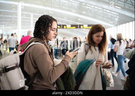 Due donne viaggiatrici controllano i loro telefoni in mezzo alla folla affollata dell'aeroporto. Foto Stock