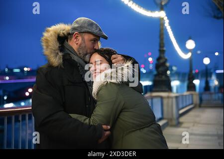 Padre e figlia condividono un caldo e affettuoso abbraccio su un ponte illuminato a Londra durante la sera. Foto Stock