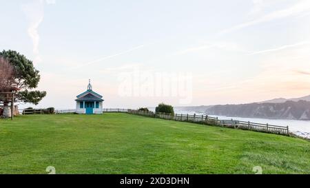 Un tranquillo paesaggio costiero caratterizzato da una piccola cappella sullo sfondo di un tramonto Foto Stock