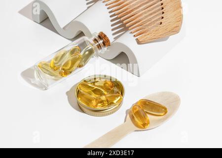 I contenitori in vetro trasparente e un cucchiaio di legno contengono capsule Omega 3 dorate, posizionate su uno sfondo bianco per un look pulito e moderno Foto Stock