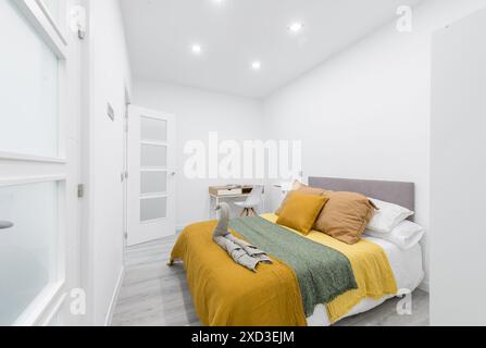 Camera da letto elegante e moderna dallo stile minimalista con un tocco vivace. La camera è decorata con una comoda testata grigia, pareti bianche e fresche, una Foto Stock