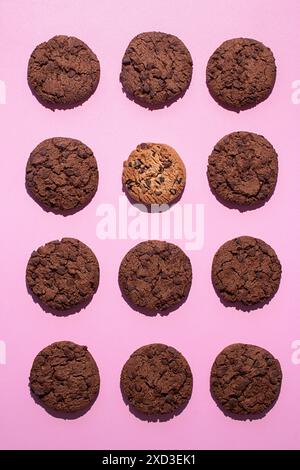 Fotografie piatte di dodici biscotti a goccia di cioccolato doppi disposti su un vivace sfondo rosa Foto Stock