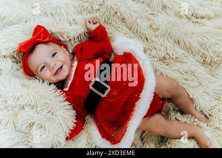 Dall'alto, la bambina vestita con un abito natalizio rosso con un fiocco giace su una morbida coperta Foto Stock