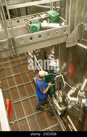 Un lavoratore controlla le vasche di fermentazione in acciaio inossidabile in un'azienda vinicola contemporanea, mescolando tradizione con metodi moderni di vinificazione Foto Stock