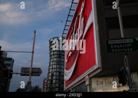 Il Neon, Kings Cross Coca-Cola cartello ravvicinato guardando in alto lungo Victoria Street verso l'alto edificio di appartamenti OMNIA, illuminato e illuminato Foto Stock