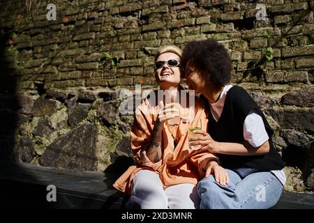 Due donne diverse, che si godono un appuntamento in un accogliente caffè, sedute fianco a fianco. Foto Stock