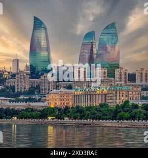 Vista notturna delle iconiche torri illuminate delle fiamme a Baku, Azerbaigian, la moderna architettura degli edifici si riflette nelle calme acque del Mar Caspio Foto Stock