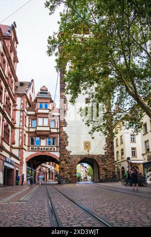 Freiburg im Breisgau, Germania, 23 luglio 2023, ingresso antico martinstor alla città vecchia con il ristorante mc Donalds accanto e binari del tram Foto Stock