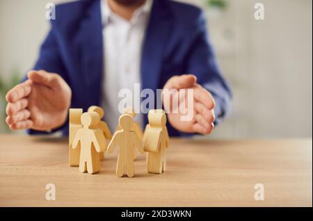 Uomo d'affari che tiene per mano persone di legno in piedi alla scrivania che proteggono i diritti umani Foto Stock