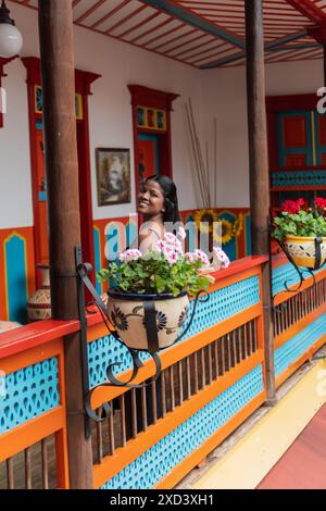 donna sorridente che posa in una vibrante casa coloniale decorata con vasi di fiori. Foto Stock