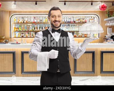 Cameriere sorridente che tiene in mano un piatto di torta vuoto in un bar Foto Stock