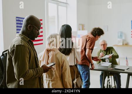 Giovane cittadino afroamericano che tiene lo smartphone in fila alla stazione elettorale il giorno delle elezioni, copia spazio Foto Stock
