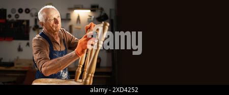 Un uomo anziano con guanti arancioni e grembiule blu sabbiano una vecchia sedia di legno in un'officina. È nel suo laboratorio e si concentra sulla preparazione della sedia Foto Stock