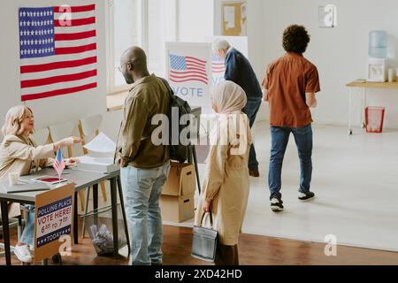 Visione ad angolo alto ampio di cittadini diversi che prendono le schede elettorali e votano al seggio elettorale il giorno delle elezioni, copia spazio Foto Stock