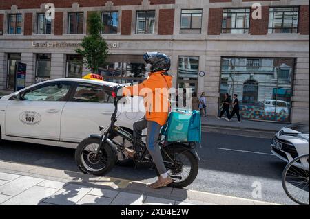 Consegna del cibo in bicicletta elettrica in attesa al semaforo nel centro di Leeds in una calda giornata estiva Foto Stock
