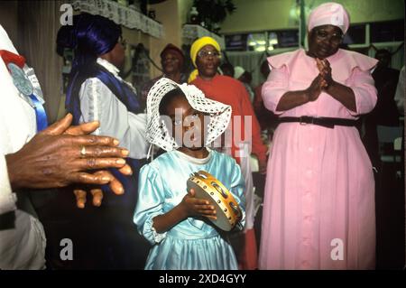 Suona tamburello una giovane ragazza nera britannica che fa musica, partecipa a una messa in chiesa di metà settimana. Mount Zion Spiritual Baptist Church Kensal Green, Londra, Inghilterra 1990.1990s UK HOMER SYKES Foto Stock