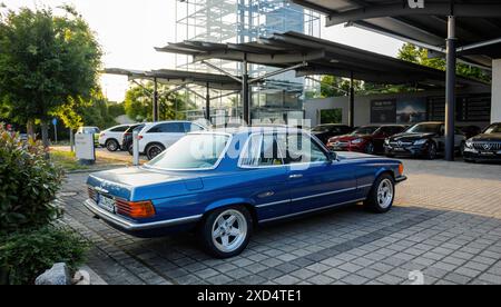 Kehl, Francia - 27 maggio 2023: Una Mercedes-Benz 450 SLC blu parcheggiata fuori da una concessionaria Mercedes-Benz, che presenta il classico modello di telaio W107. Le moderne auto Mercedes-Benz sono visibili sullo sfondo, evidenziando l'eredità e l'evoluzione del marchio Foto Stock