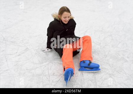 Cadere mentre si pattina su una pista di pattinaggio. Una ragazza di 11-12 anni cade sul ghiaccio. Foto Stock