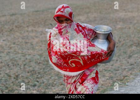 20 giugno 2024, Dacca, Dacca, BANGLADESH: Una donna del Bangladesh che trasporta acqua potabile dopo averla raccolta da una fonte di acqua dolce, camminando molto per raccogliere acqua potabile nella zona costiera di Khulna, Bangladesh. Secondo una ricerca dell'American Geophysical Union, l'innalzamento del livello del mare, che sta influenzando la disponibilità di acqua potabile pulita, causerà la migrazione di circa 1,3 milioni di persone in tutto il paese entro il 2050. Una combinazione di inondazione delle maree, inondazione delle tempeste e intrusione di acqua salata sta portando a un aumento della salinità nelle acque sotterranee e nello stagno di acqua dolce Foto Stock