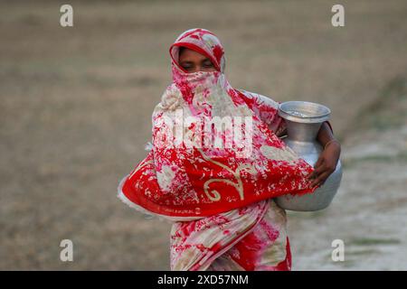 20 giugno 2024, Dacca, Dacca, BANGLADESH: Una donna del Bangladesh che trasporta acqua potabile dopo averla raccolta da una fonte di acqua dolce, camminando molto per raccogliere acqua potabile nella zona costiera di Khulna, Bangladesh. Secondo una ricerca dell'American Geophysical Union, l'innalzamento del livello del mare, che sta influenzando la disponibilità di acqua potabile pulita, causerà la migrazione di circa 1,3 milioni di persone in tutto il paese entro il 2050. Una combinazione di inondazione delle maree, inondazione delle tempeste e intrusione di acqua salata sta portando a un aumento della salinità nelle acque sotterranee e nello stagno di acqua dolce Foto Stock