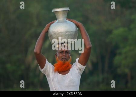 20 giugno 2024, Dacca, Dacca, BANGLADESH: Un uomo bengalese che trasporta acqua potabile dopo averla raccolta da una fonte di acqua dolce, camminando molto per raccogliere acqua potabile nella zona costiera di Khulna, Bangladesh. Secondo una ricerca dell'American Geophysical Union, l'innalzamento del livello del mare, che sta influenzando la disponibilità di acqua potabile pulita, causerà la migrazione di circa 1,3 milioni di persone in tutto il paese entro il 2050. Una combinazione di inondazioni mareali, inondazioni di tempeste e intrusioni di acqua salata sta portando a un aumento della salinità nelle acque sotterranee e negli stagni di acqua dolce, Foto Stock