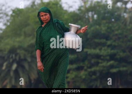 20 giugno 2024, Dacca, Dacca, BANGLADESH: Una donna del Bangladesh che trasporta acqua potabile dopo averla raccolta da una fonte di acqua dolce, camminando molto per raccogliere acqua potabile nella zona costiera di Khulna, Bangladesh. Secondo una ricerca dell'American Geophysical Union, l'innalzamento del livello del mare, che sta influenzando la disponibilità di acqua potabile pulita, causerà la migrazione di circa 1,3 milioni di persone in tutto il paese entro il 2050. Una combinazione di inondazione delle maree, inondazione delle tempeste e intrusione di acqua salata sta portando a un aumento della salinità nelle acque sotterranee e nello stagno di acqua dolce Foto Stock