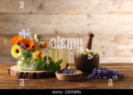 Diversi fiori e bottiglie di oli essenziali su tavola di legno Foto Stock