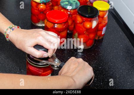 Una donna sale pomodori rossi maturi in vasetti di vetro, arrotolando il coperchio di metallo con una macchina. Prepariamo le verdure per l'inverno. Foto Stock