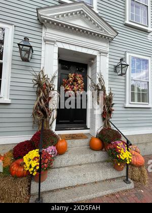 Una corona autunnale su una porta di una casa di Salem, Massachusetts, è circondata da gambi di mais, zucche e mamme in un giorno d'autunno vicino ad Halloween Foto Stock