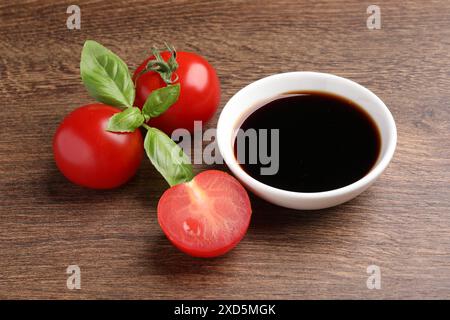 Aceto balsamico nel recipiente, basilico e pomodori su un tavolo di legno Foto Stock