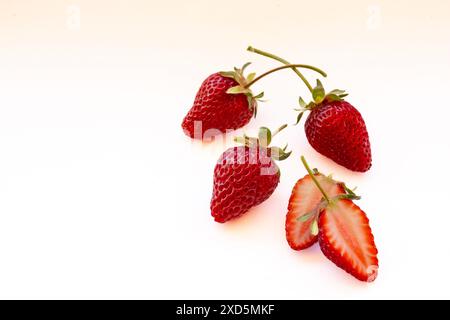 Tre fragole organiche intere raccolte a mano e una tagliata a metà, isolata su sfondo bianco con spazio di testo Foto Stock