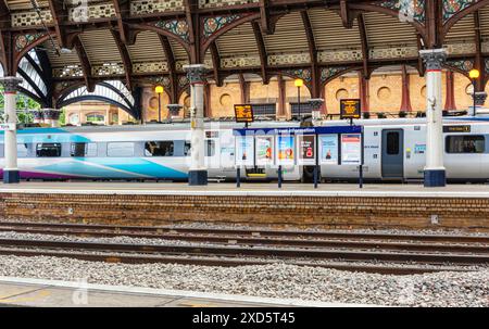 Un treno moderno si trova in una storica piattaforma della stazione ferroviaria sotto una tettoia di ferro del XIX secolo. Una bacheca con le schermate di partenza sono sul platfo Foto Stock