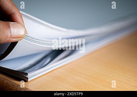 Primo piano di una mano che sfoglia le pagine di un libro o di una rivista su una superficie di legno. Foto Stock