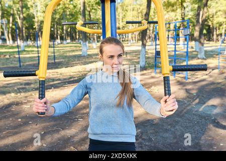 La ragazza sportiva è impegnata nel fitness all'aperto su simulatori sportivi e allena i muscoli della schiena Foto Stock