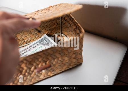 Una mano che apre un piccolo cestello in tessuto contenente una banconota da un dollaro, collocato su una superficie bianca. Foto Stock