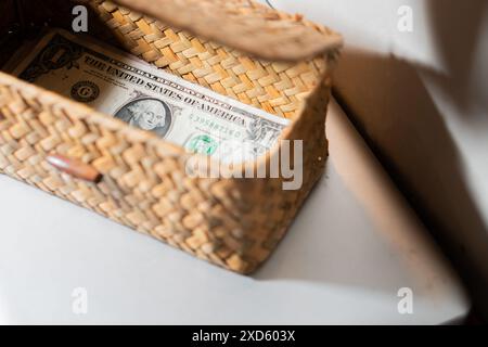 Un cestino in tessuto contenente una banconota da un dollaro, collocato su una superficie bianca. Foto Stock