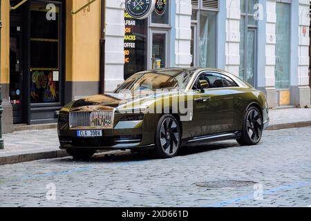 Una Rolls-Royce Spectre completamente elettrica parcheggiata in una strada acciottolata nel centro di Praga con edifici storici e negozi moderni sullo sfondo Foto Stock