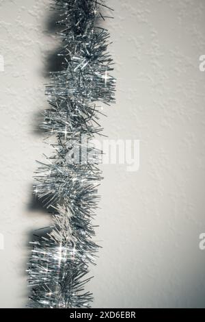 Tinsel argento brillante contro parete bianca, sfondo Foto Stock