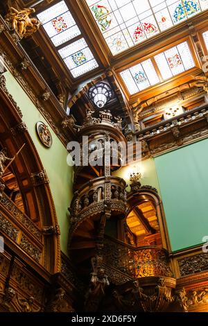 Sinaia, Romania - 26 agosto 2022: Scala a chiocciola intagliata in legno nella Hall of Honor all'interno del castello di Peles. Il ricco interno del Peles National Foto Stock