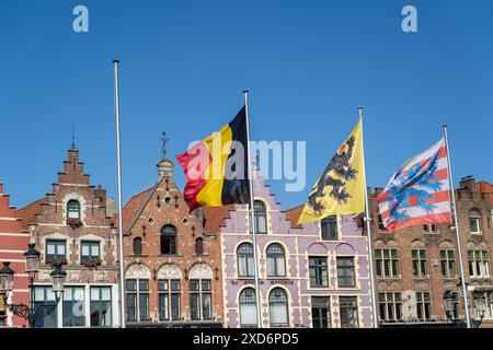 Fotografia della piazza del mercato nel centro di Brugges, Belgio, con bandiere sugli alberi e negozi e caffetterie locali sullo sfondo Foto Stock