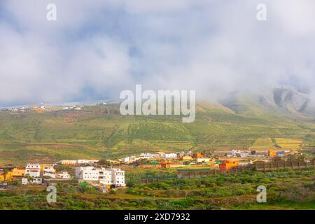 Piccola cittadina con poche case situata sulla verde montagna. Il cielo è nuvoloso e il sole non è visibile. Paesaggio di campagna di Gran Canaria Foto Stock